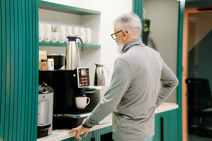 An older man making himself coffee at the renovated medical office space
