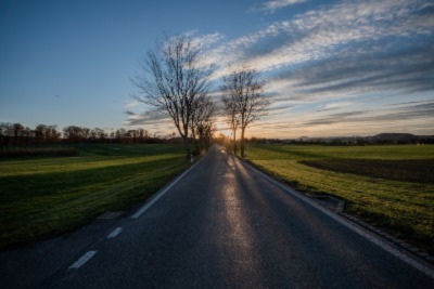 a road surrounded by grass during sunset with the couple of trees