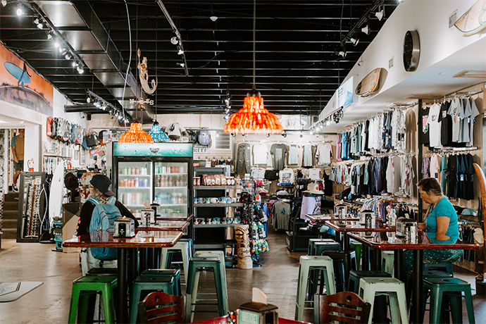 a shop with with clothes, tables and chairs, people sitting at the tables waiting, a fridge with drinks