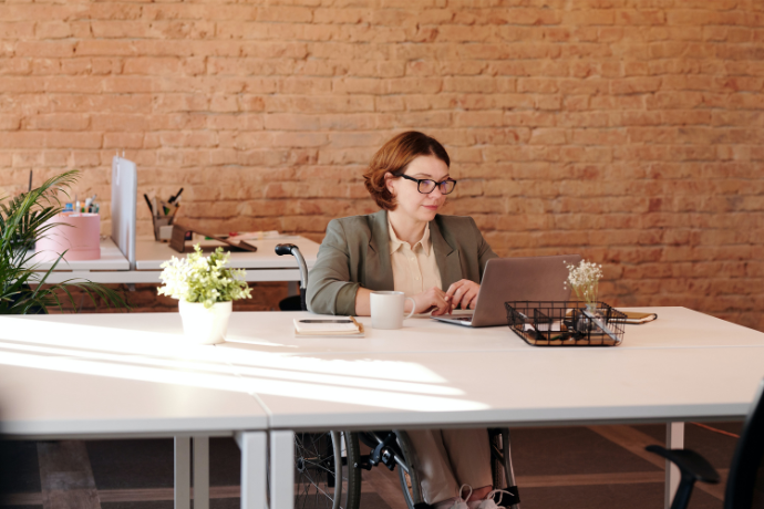a woman sitting at the table in the wheelchair and working on her laptop