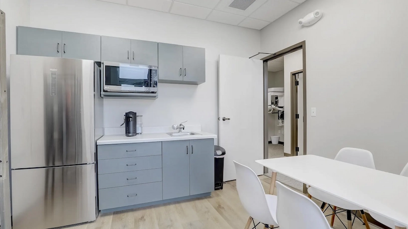 New employee break room with grey-blue cabinetry, oak flooring, and stainless steel appliances