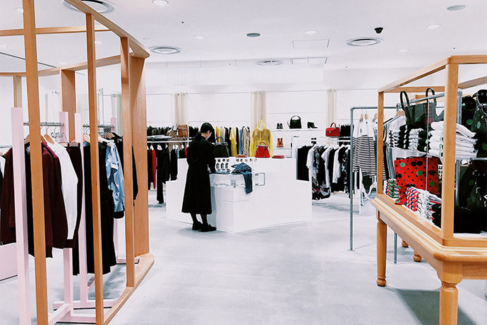 big white clothes store with clothes hanging on wooden racks and a person in the middle looking at things