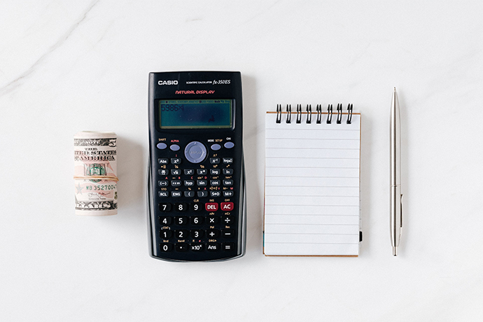 Roll of money, calculator, notepad, and a pen located on white table
