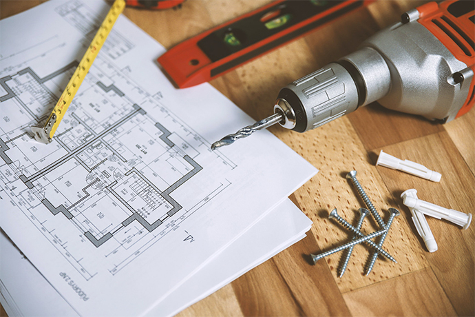 a drill, nails, commercial construction plan, and measuring tape on the desk