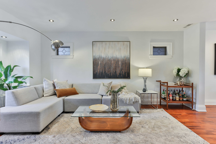 grey sectional with the abstract picture behind, coffee table in the middle, hardwood flooring with the rug in the couch area