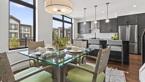 Interior photo of a dining room with glass table and kitchen with stainless steel appliances