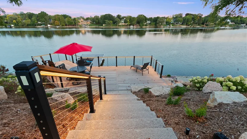 Newly built deck overlooking a beautiful lake. Black deck furniture and a red umbrella are on the deck.
